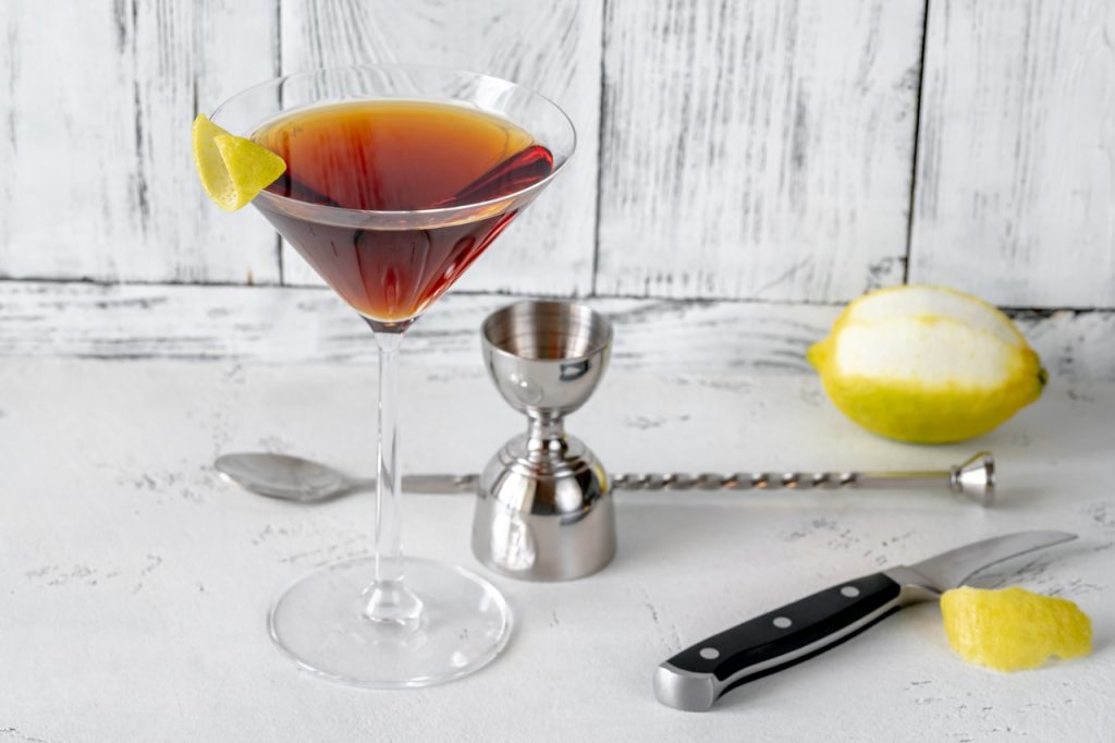 A glass of Martinez cocktail, with a stirrer and a jigger.