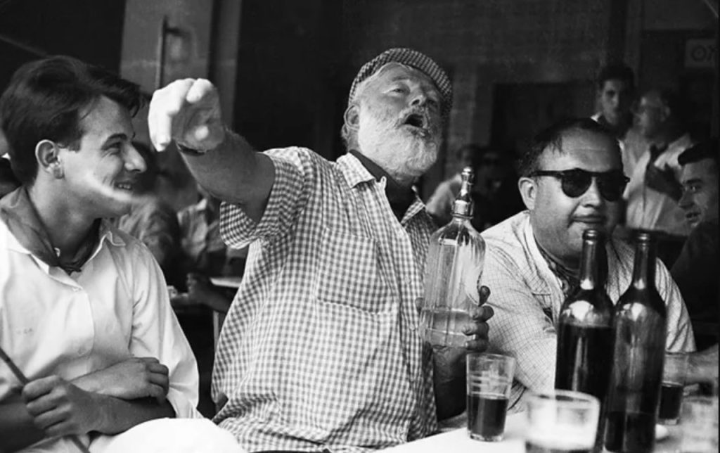 The writer Hemingway with some friends drinks and talks while sitting at a bar in Cuba