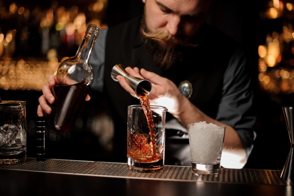 Hands of a barman using a jigger to dose a cocktail.