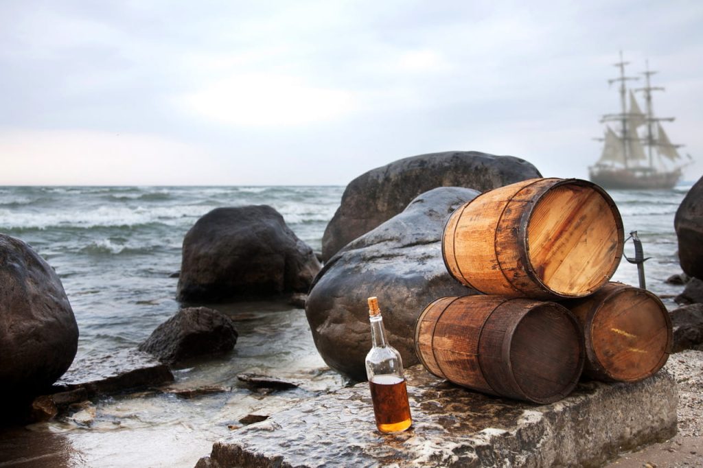 Rum barrels on a beach with a pirate sailing ship in the background