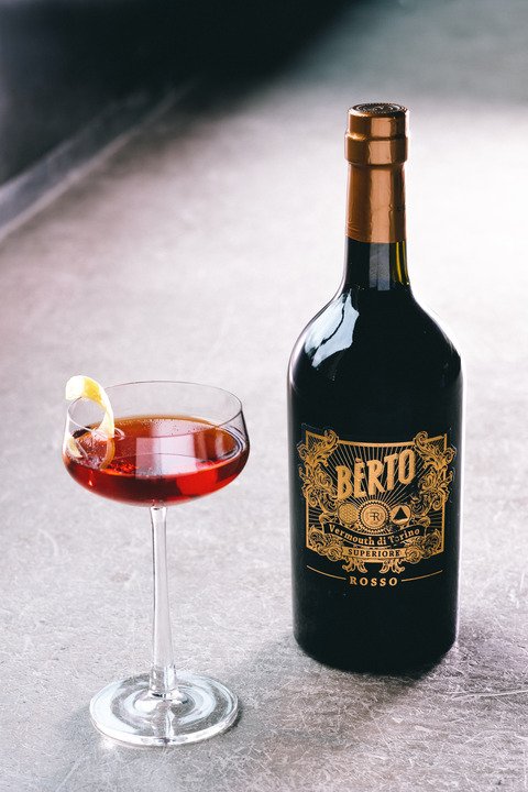 A bottle of Vermouth Rosso Bèrto and a glass full of it, on a table.